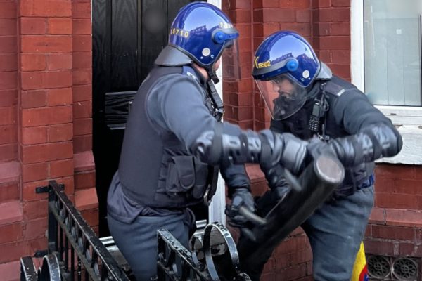 Police battering a door down on Levenshulme Road, Gorton. Image: GMP